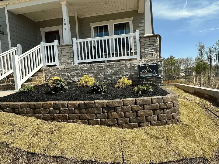 A curved block retaining wall surrounding the garden beside a front porch.
