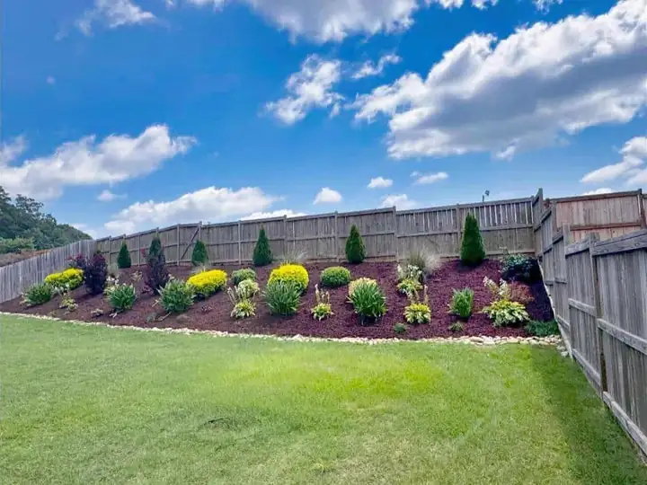 Lawn and planted garden beds along a backyard fence.