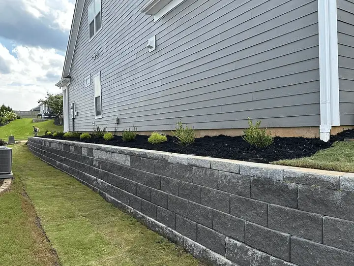A long block retaining wall and mulched planting bed beside a house.