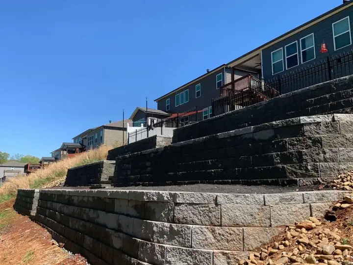 Tiered block retaining walls across a sloped yard behind homes.